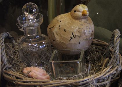 Mand gevuld met glazen flesje, theelicht, houten vogel en rozenzeepje.