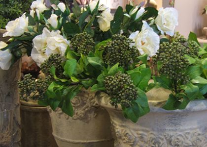 Kunstbloemschikking met witte wilde rozen, groen blad en skimmia in grove aardewerken pot.