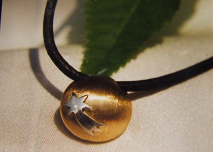 Bolvormige ashanger in geelgoud met een zilveren vallende ster in reliëf.