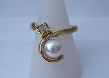 Prachtige geelgouden ring met witte parel in krul en groene steen in zetting.